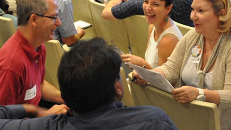 Faculty members sit together discussing and laughing